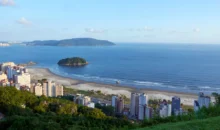 Vista aérea da cidade de Santos, localizada no litoral do estado de São Paulo, Brasil, com prédios e áreas verdes visíveis. A fotografia ilustra a questão do aquecimento dos oceanos que desafia as cidades costeiras.