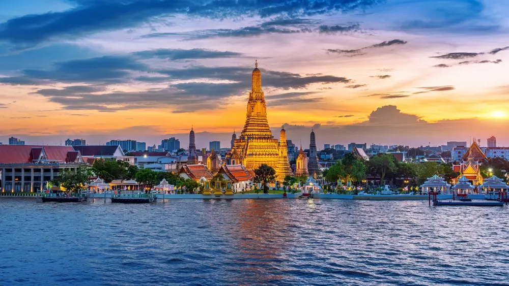 Bangkok ao entardecer, destacando a arquitetura tradicional com vistas para o rio, ideal para quem busca um cenário inspirador de trabalho remoto.