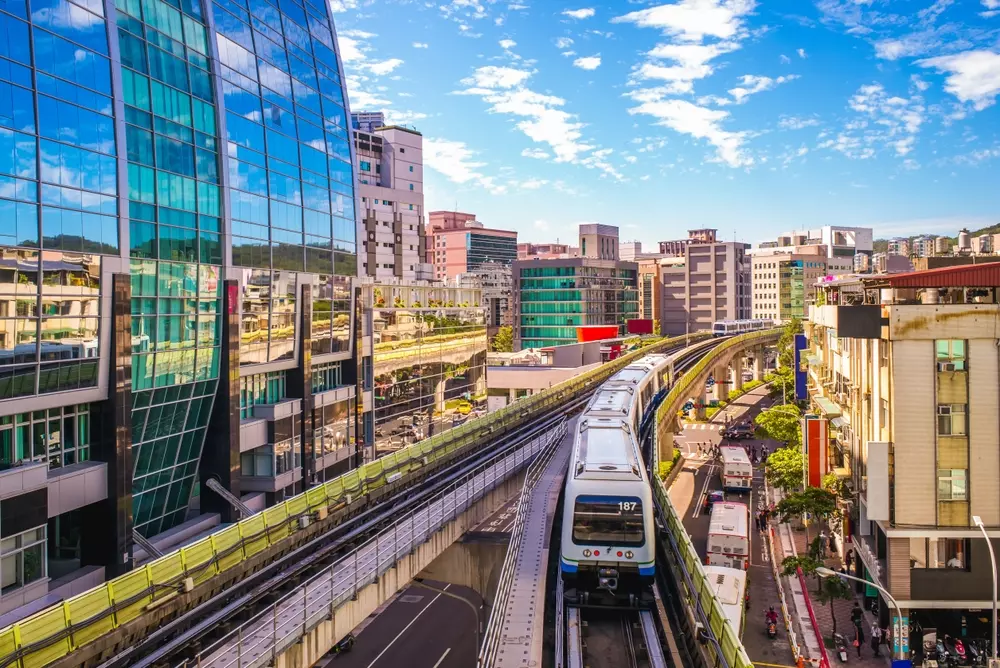 	
Paisagem urbana em Taipei com edifícios modernos, transporte público e infraestrutura avançada sob um céu azul claro.