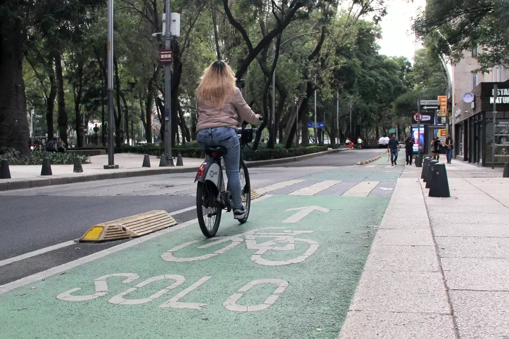 Pessoa pedalando bicicleta na ciclofaixa na Cidade do México, promovendo a caminhabilidade e mobilidade urbana sustentável em uma rua arborizada.