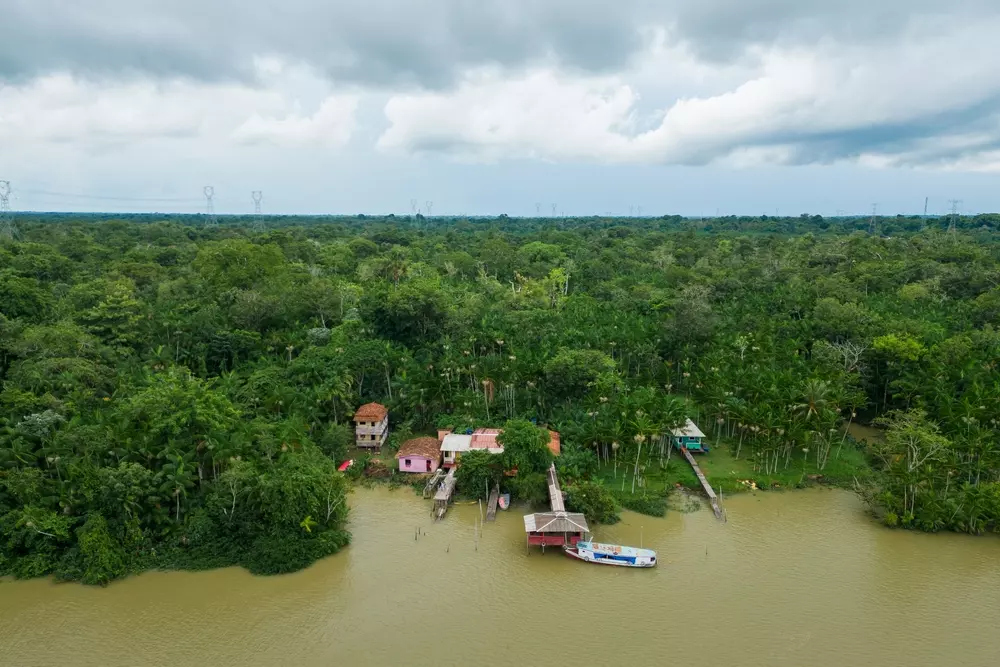 Comunidade ribeirinha isolada na floresta amazônica com casas à beira do rio e barcos ao lado, destacando a vida nas comunidades ribeirinhas.