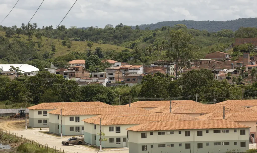 Habitações populares em uma área com vegetação ao fundo, destacando a crise habitacional em regiões em desenvolvimento.