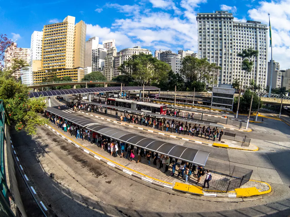 Pessoas esperando em um terminal de ônibus na cidade de São Paulo, destacando a mobilidade urbana e acessibilidade na cidade.