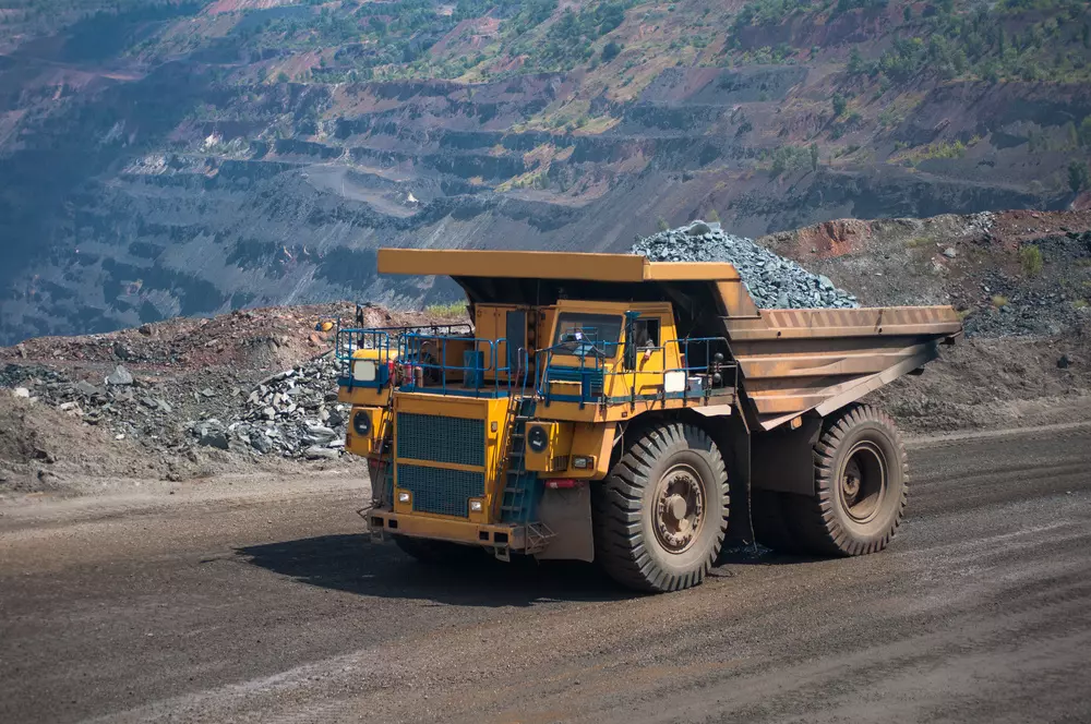 Caminhão de mineração transportando rejeitos de mineração em uma obra de mineração a céu aberto com paisagem de montanhas ao fundo.