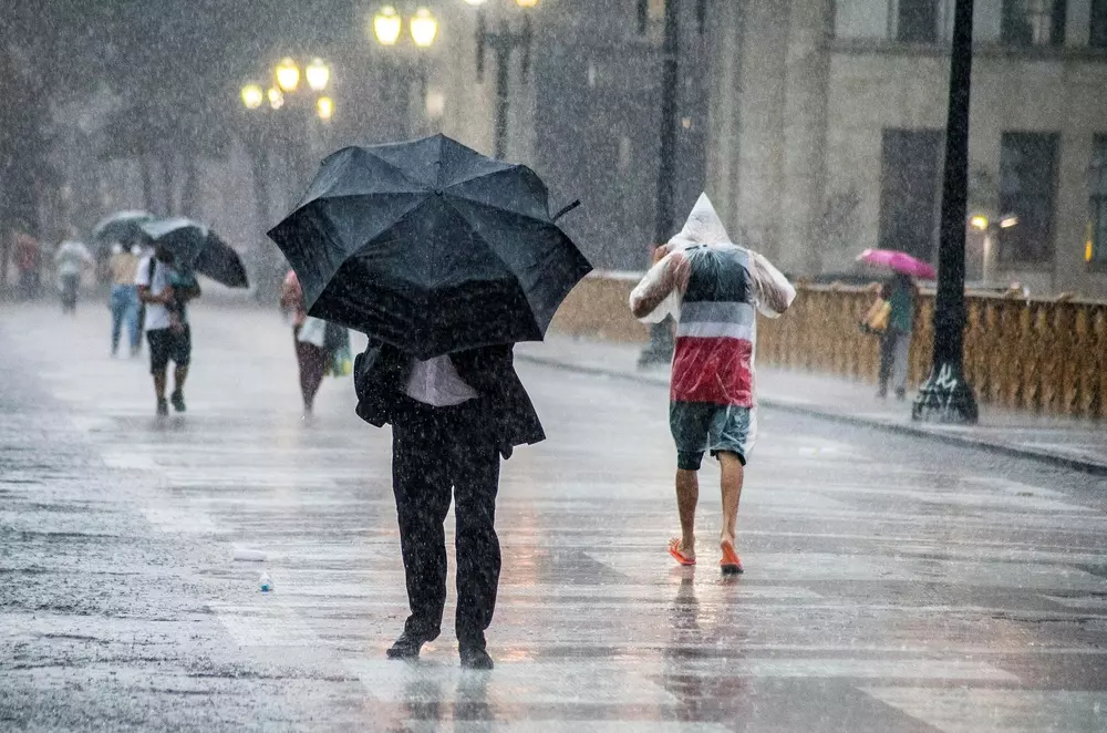Pessoas caminhando com guarda-chuvas na rua durante uma forte chuva, cenário urbano com tempo chuvoso e molhado, ambiente da cidade de São Paulo em dia de chuva.