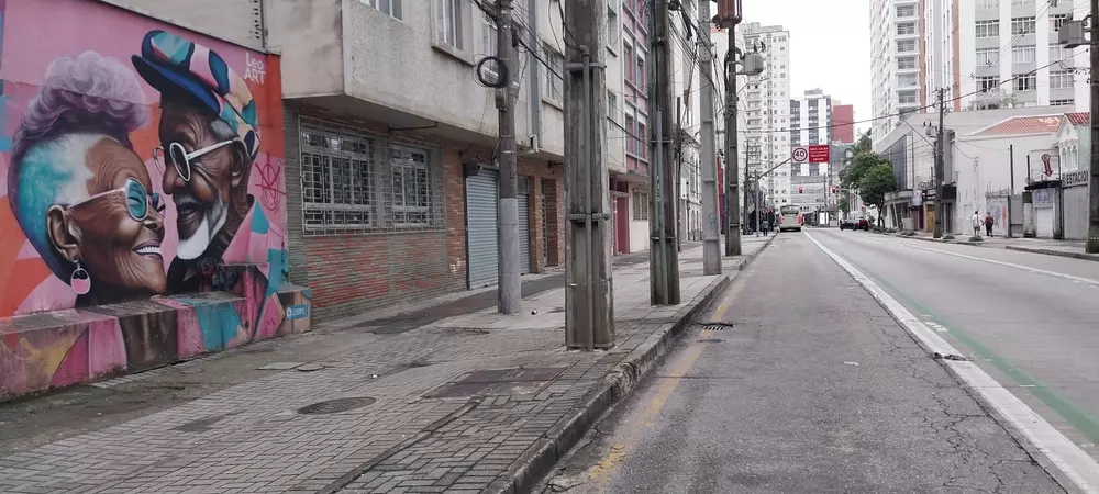 Vista de uma rua urbana com uma parede de grafite colorido em estilo street art, destacando idosos sorridentes e felizes