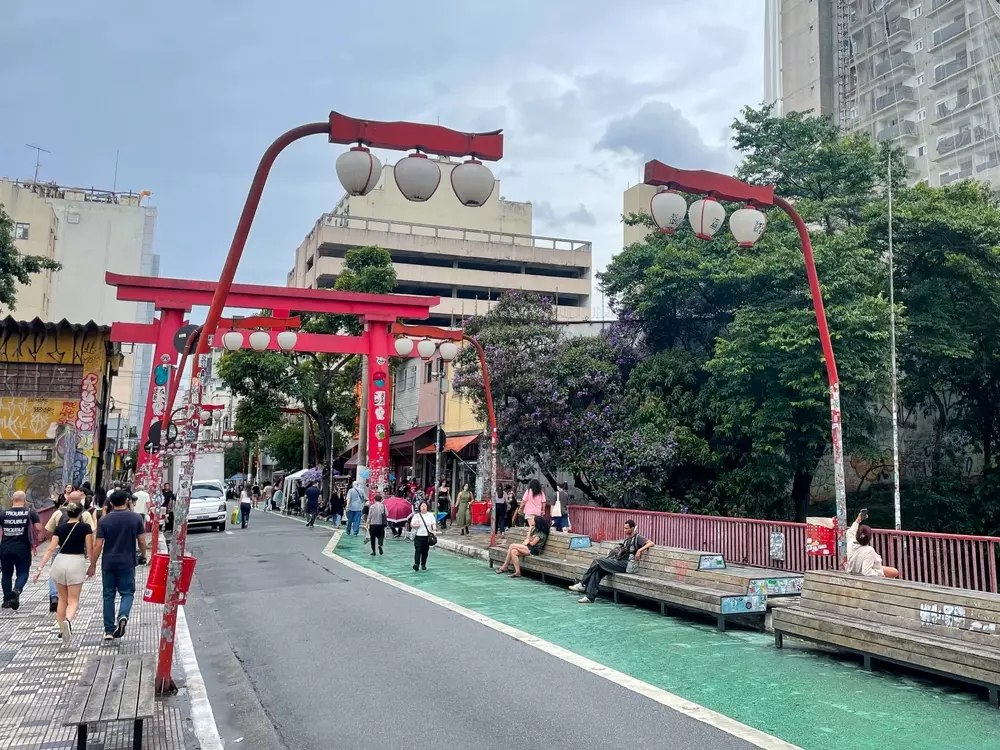 Rua aberta na Liberdade em São Paulo com iluminação tradicional japonesa, árvores e pessoas caminhando, promovendo cultura e convivência no bairro.