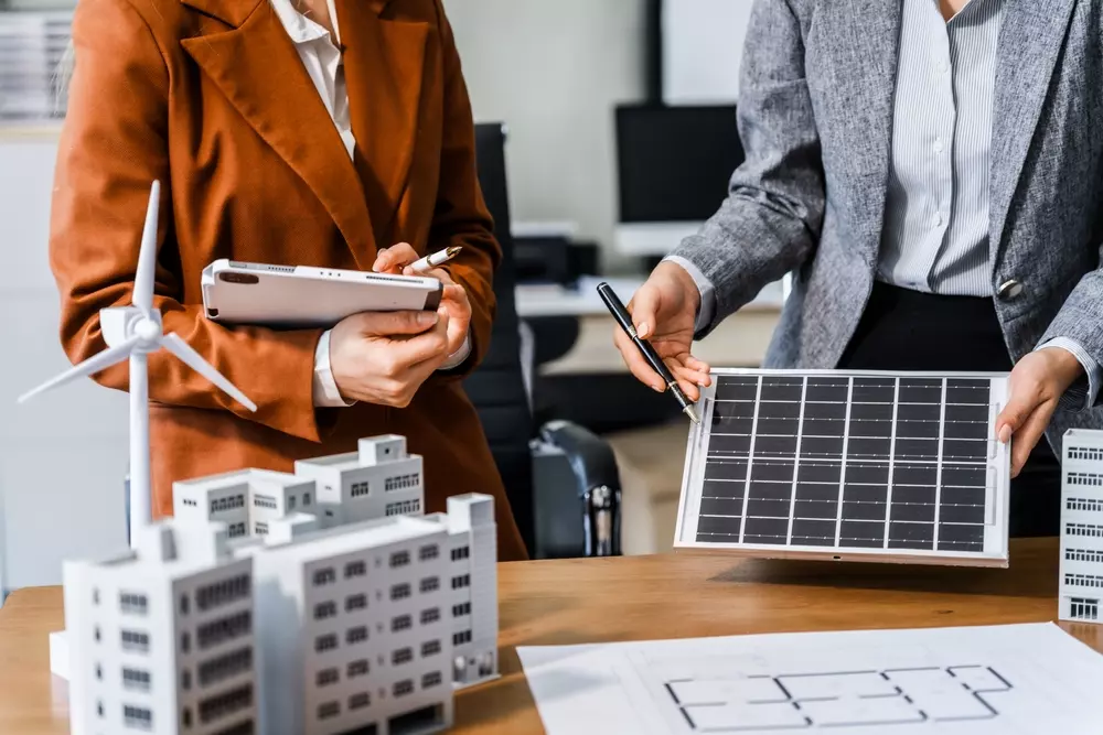 Duas pessoas analisando soluções sustentáveis para ambientes internos, incluindo energia solar e ventilação, para prevenir a Síndrome do Edifício Doente.