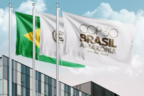 Bandeiras do Brasil e da COP Brasil Amazônia tremulam em frente a um prédio moderno durante o evento COP30 em Belém, onde foram estabelecidos os primeiros padrões globais para edificações sustentáveis e resilientes.