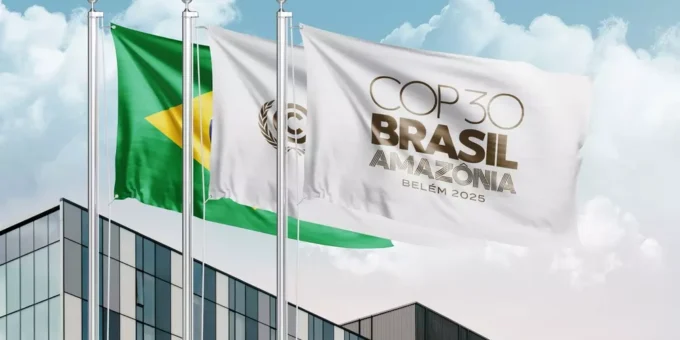 Bandeiras do Brasil e da COP Brasil Amazônia tremulam em frente a um prédio moderno durante o evento COP30 em Belém, onde foram estabelecidos os primeiros padrões globais para edificações sustentáveis e resilientes.