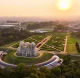 Pôr do sol no horizonte de Curitiba com vista aérea de um bairro sustentável, destacando jardins bem planejados e uma estufa moderna na paisagem