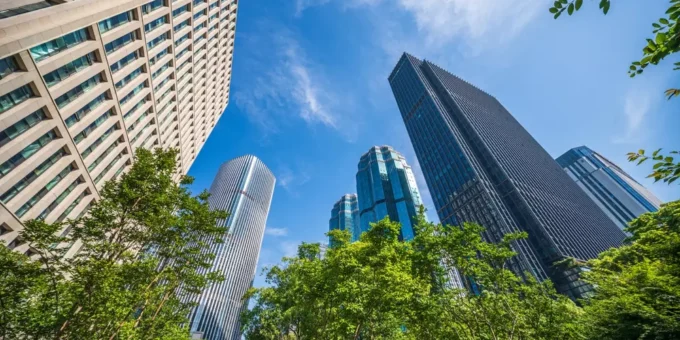 Arranha-céus modernos em uma área urbana, com árvores verdes na frente e céu azul ao fundo, destacando a importância do Estatuto da Cidade na organização urbana.