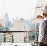 Profissional de construção civil analisando projeto de Lean Construction em um ambiente moderno de escritórios com vista para a cidade