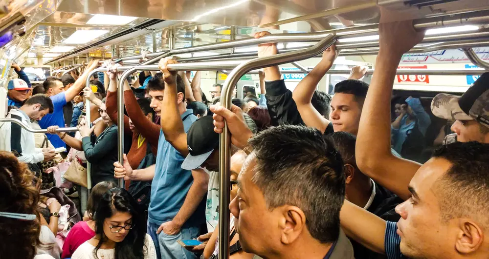 um transporte público lotado com muitas pessoas dentro, segurando as barras de apoio, mostrando a rotina diária de quem usa o metrô ou ônibus na cidade