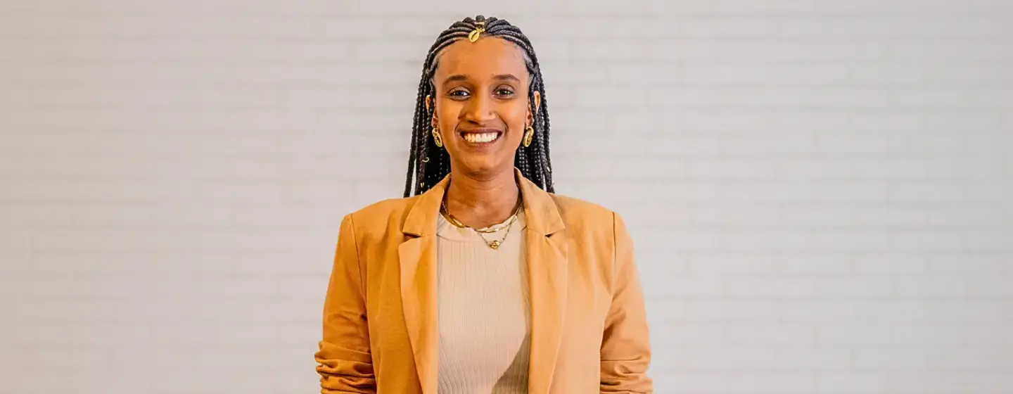 Audrey Carolini, arquiteta, urbanista e designer, posando com sorriso e vestindo blazer bege ao lado de parede neutra