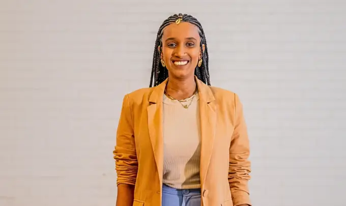 Audrey Carolini, arquiteta, urbanista e designer, posando com sorriso e vestindo blazer bege ao lado de parede neutra