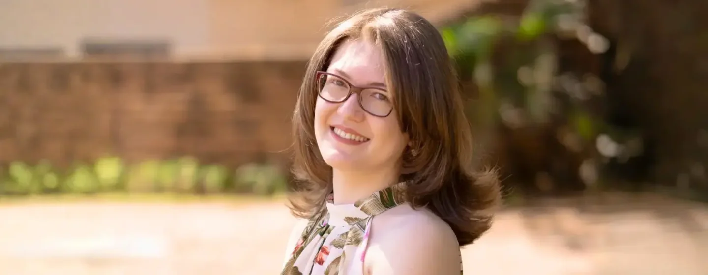 Retrato de Karla Zambrano sorridente ao ar livre, com fundo desfocado, usando óculos e vestido floral.