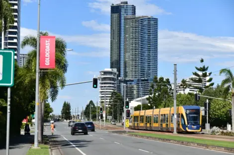 Um cenário urbano com um trem elétrico amarelo em uma via de transporte, altos prédios ao fundo e árvores, destacando a mobilidade sustentável e o uso de carros elétricos na cidade.