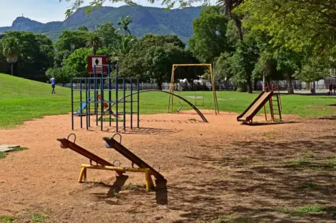 Parque com equipamentos públicos de lazer, incluindo brinquedos e estruturas de ginástica, em área verde com árvores e montanhas ao fundo
