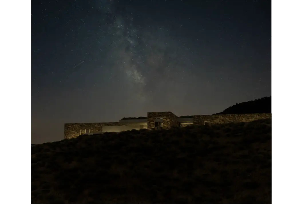 Paisagem escura com uma construção de pedra ao pé de uma colina, sob um céu estrelado, simbolizando conceitos de design regenerativo.