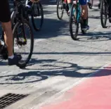 Grupo de ciclistas pedalando em ciclovia pavimentada, promovendo transporte sustentável e saúde em área urbana com sombra.