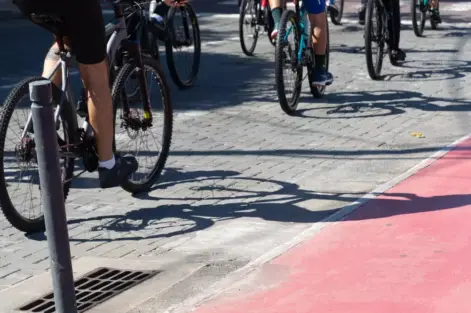 Grupo de ciclistas pedalando em ciclovia pavimentada, promovendo transporte sustentável e saúde em área urbana com sombra.