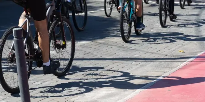 Grupo de ciclistas pedalando em ciclovia pavimentada, promovendo transporte sustentável e saúde em área urbana com sombra.