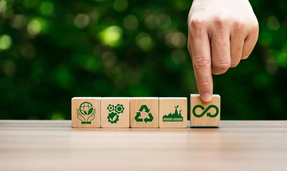 Imagem que ilustra conceitos de economia circular, com blocos de madeira representando sustentabilidade, reciclagem, reutilização e inovação, inseridos em um contexto de preservação ambiental.