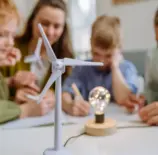 Crianças participando de uma atividade educativa sobre energias renováveis em sala de aula, com foco na adaptação climática das cidades usando fontes sustentáveis.