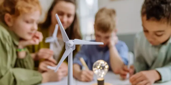 Crianças participando de uma atividade educativa sobre energias renováveis em sala de aula, com foco na adaptação climática das cidades usando fontes sustentáveis.