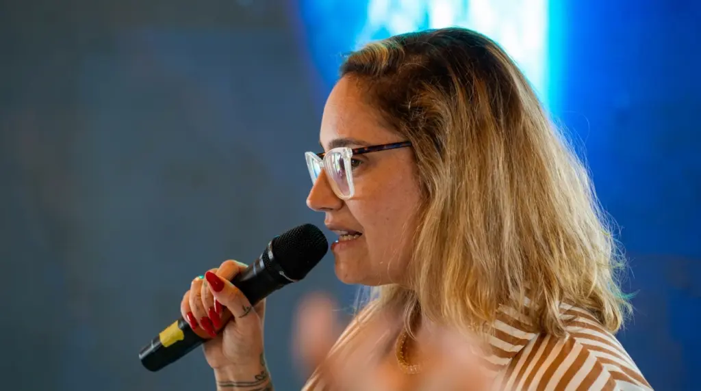 Lídice Berman, usando óculos, com um microfone na mão, pronta para falar