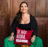 Lídice Berman sentada em um banco de madeira, apoiada em um travesseiro vermelho