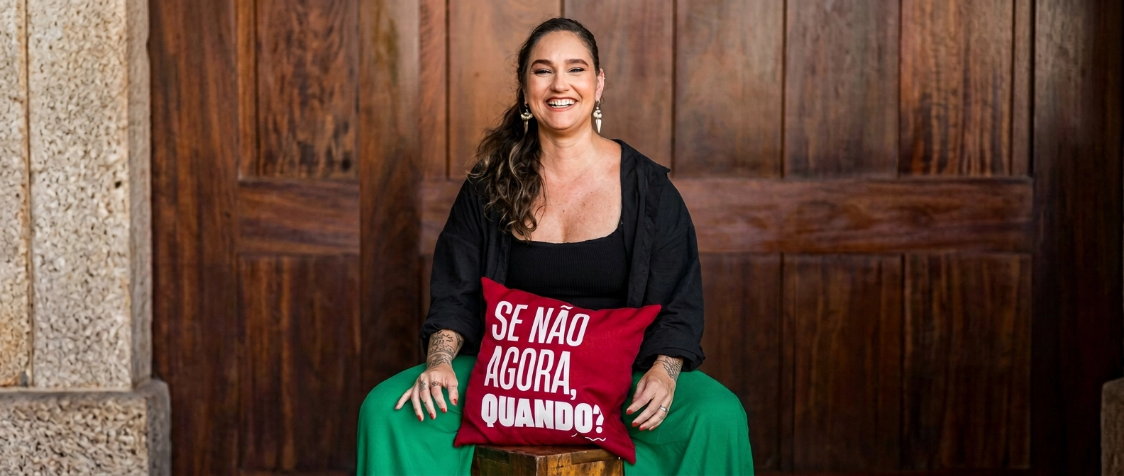 Lídice Berman sentada em um banco de madeira, apoiada em um travesseiro vermelho