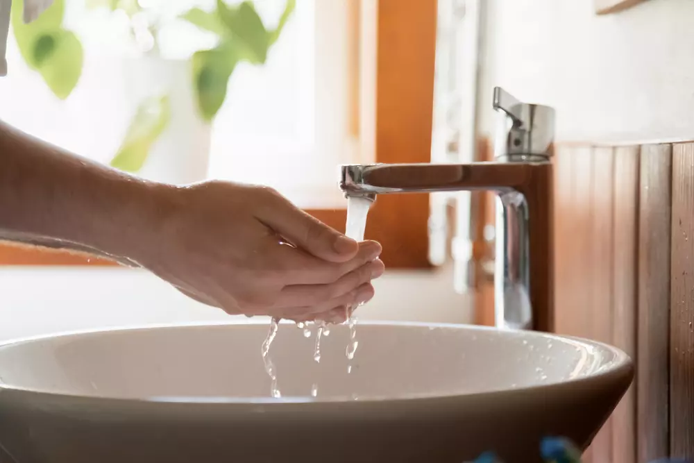 Pessoa lavando as mãos em uma pia com torneira de água limpa, promovendo hábitos de higiene essenciais para o saneamento adequado.